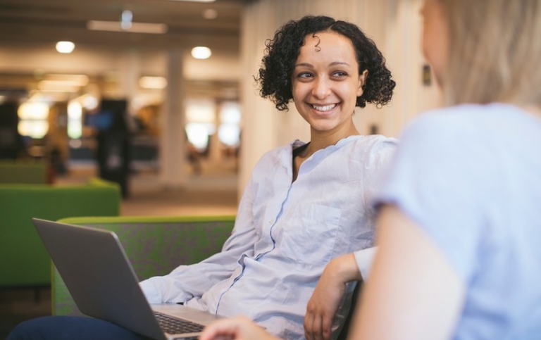 Smiling girl with a laptop talking to a friend. Photo: Niklas Björling