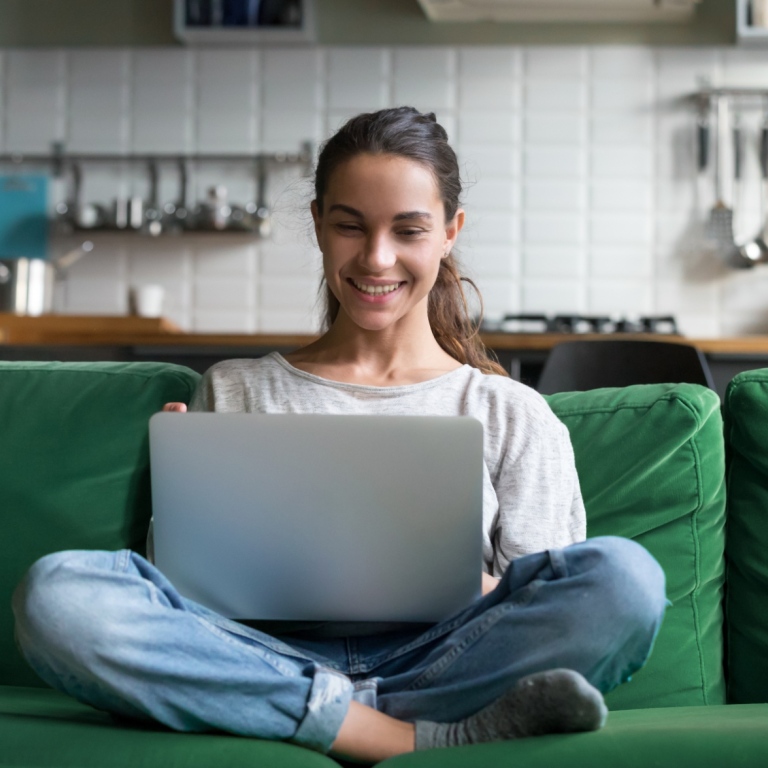 A woman with a laptop sitting on a green couch.